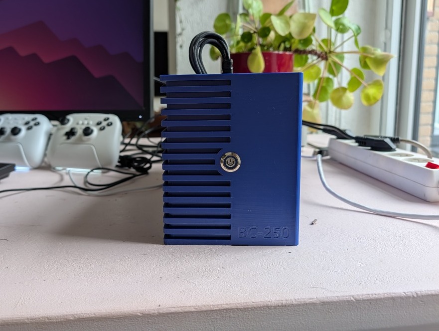 Front view of the blue 3D-printed BC-250 case with the mounted stainless power button and embossed BC-250 badge